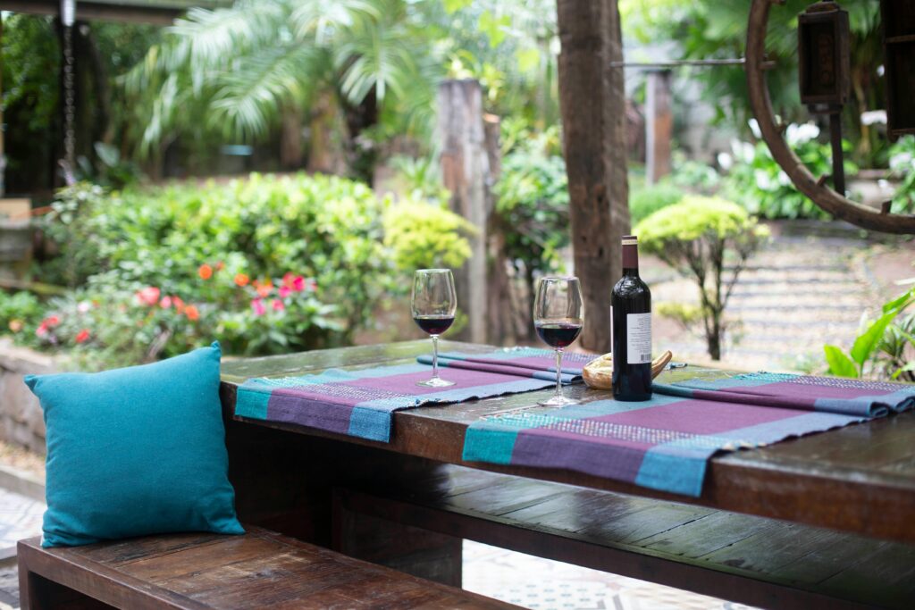 outdoor patio table Charming garden patio setting with a wooden table, wine glasses, and a bottle set for relaxation.