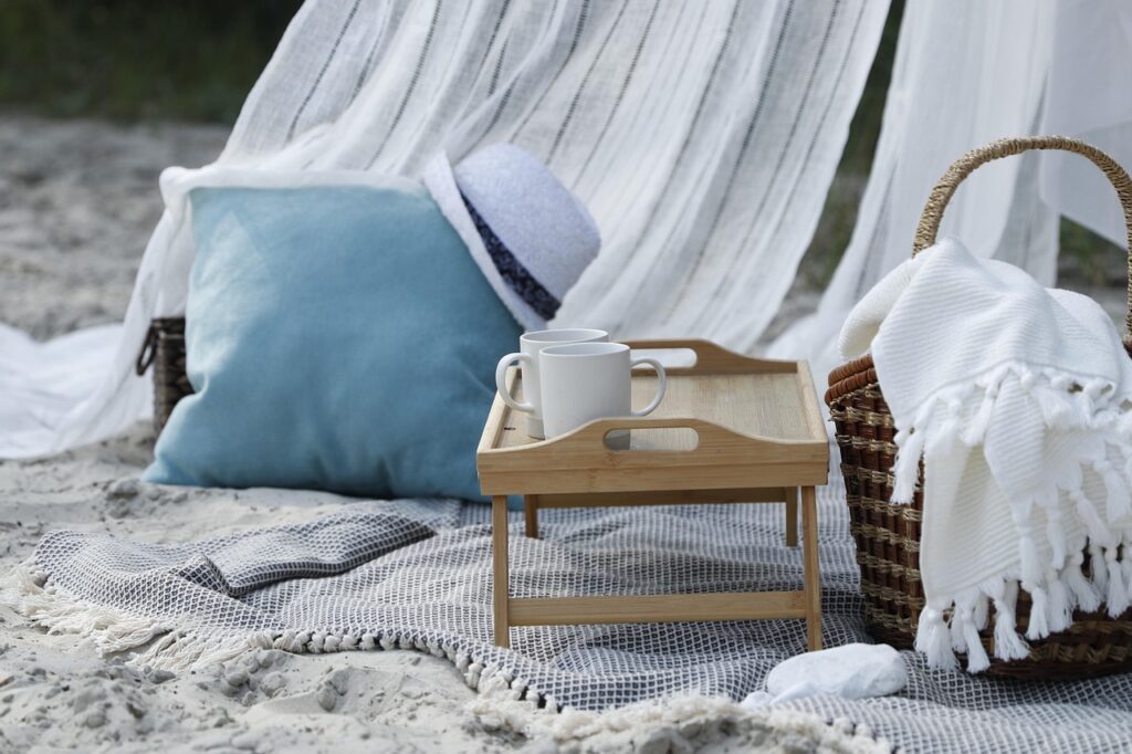 Picnic blanket with accessories A picnic blank with a small picnic basket and a table on a cozy beach.