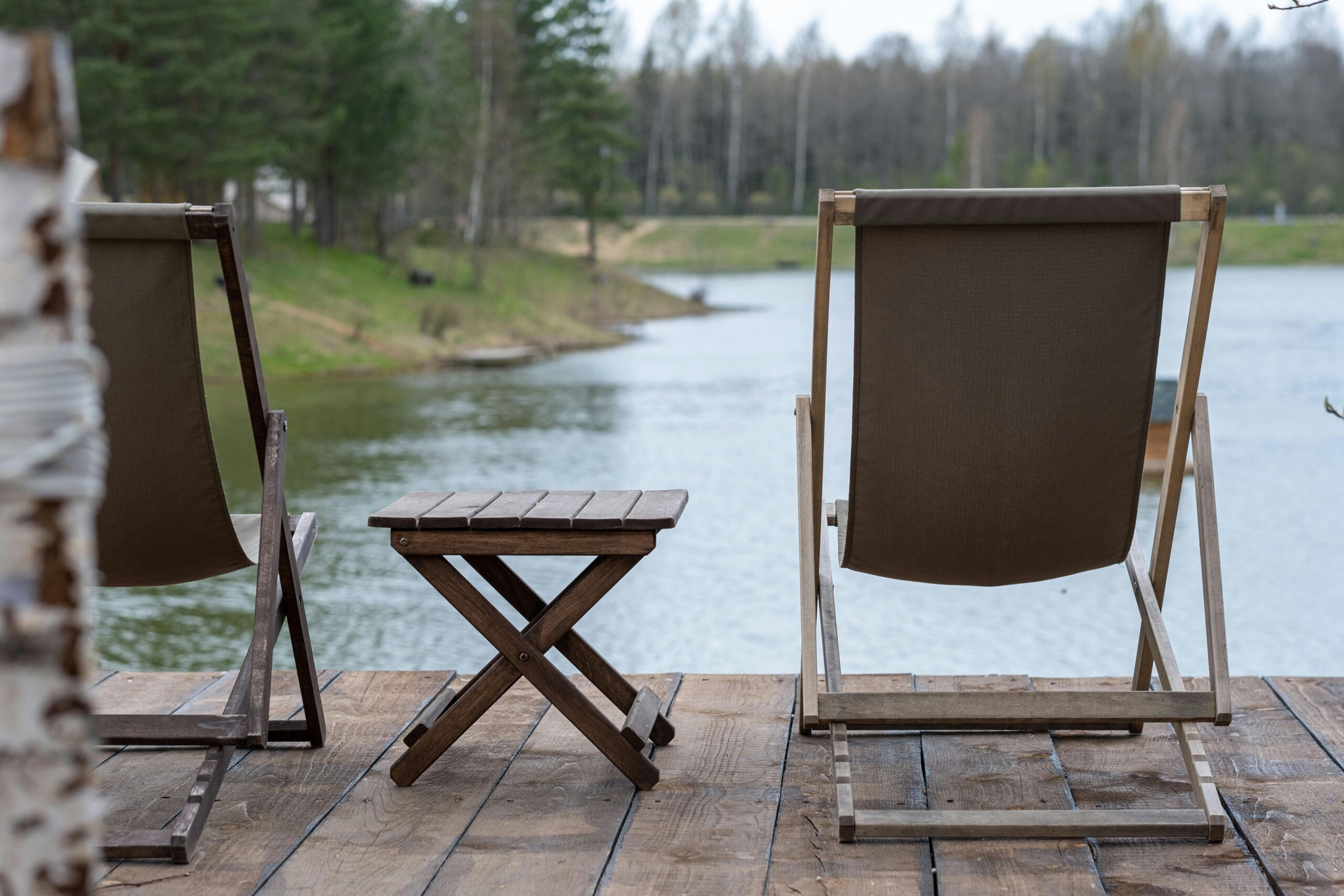 Rustic wooden deck chairs and table overlooking a serene lake and landscape.
