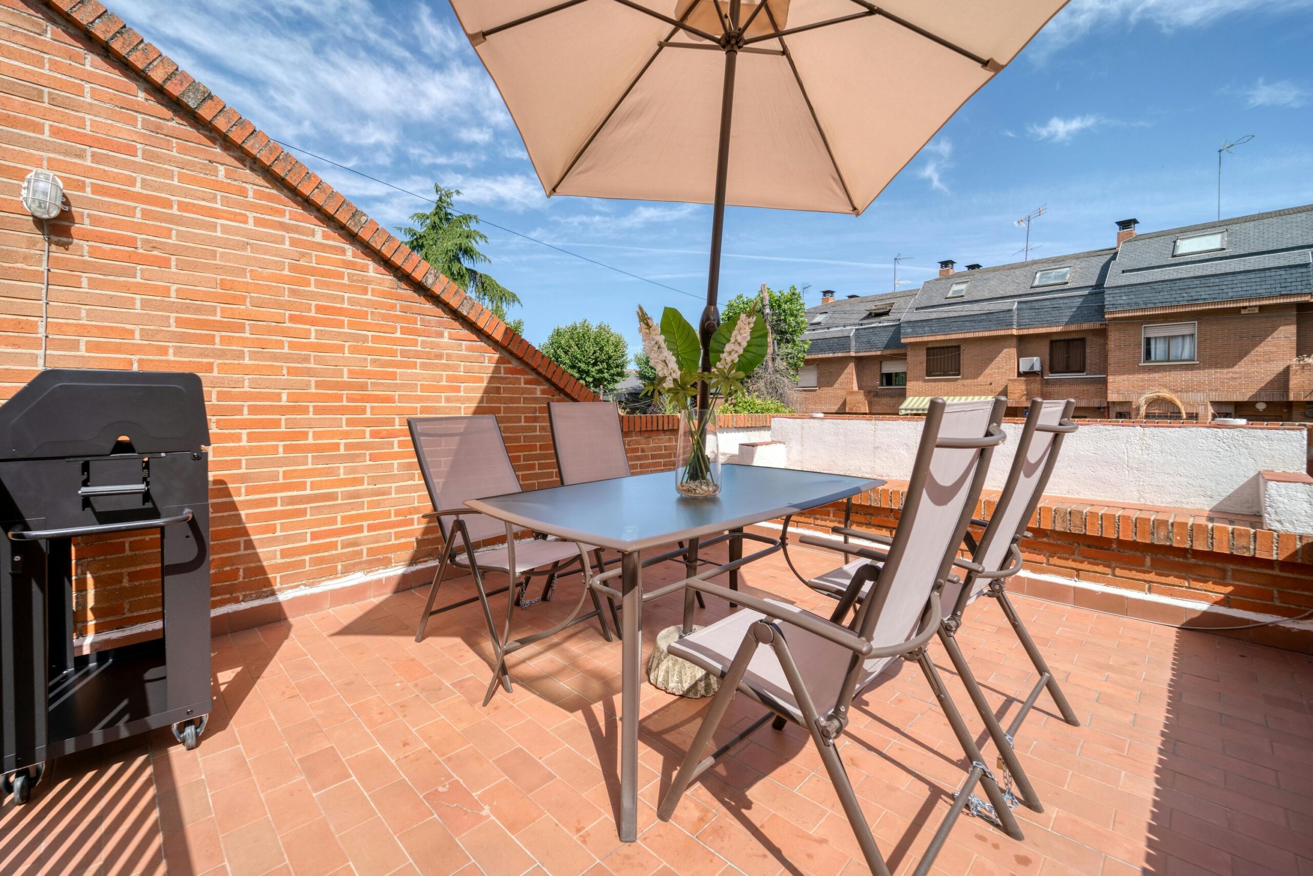 Modern terrace with table, chairs, and umbrella under the sun. Ideal summer setting.