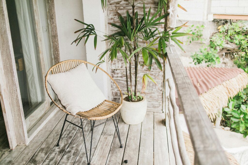 Outdoor-patio-chair Tranquil outdoor balcony area featuring a rattan chair with a cushion and vibrant green potted plant.