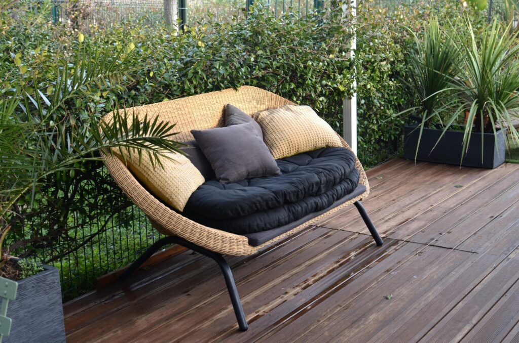 outdoor-patio-loveseat-with-pillows Comfortable stylish wicker sofa with soft seat and pillows placed in patio with lush green tropical vegetation in daytime