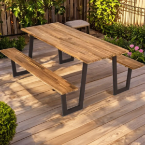 A honey-brown acacia wood picnic table in an outdoor patio setting with a wooden deck and plants.